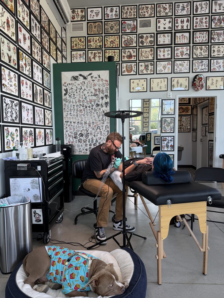 Lorin Burnett tattooing while Hank the shop dog supervises
